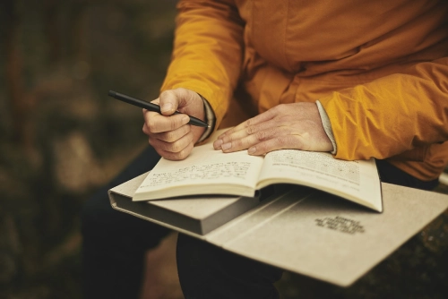 Foto delle mani di una persona mentre scrive su un taccuino.