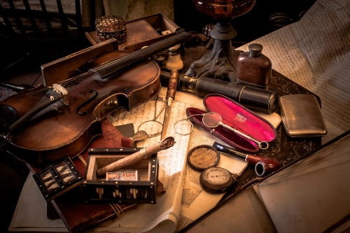 Foto di una serie di oggetti vintage, tra cui un violino, occhiali a pince-nez, una bussola, una pipa ecc. poggiati su fogli di carta scritti.