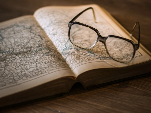 Foto di un paio di occhiali moderni poggiato su un libro aperto raffigurante una cartina geografica.
