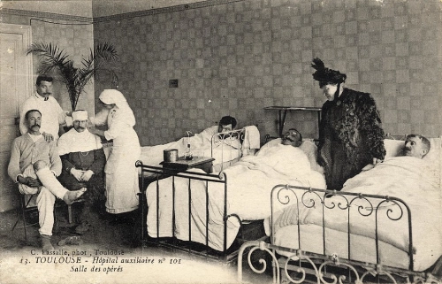 Cartolina della Prima guerra mondiale raffigurante la stanza di un ospedale con dei feriti e delle infermiere che li curano.